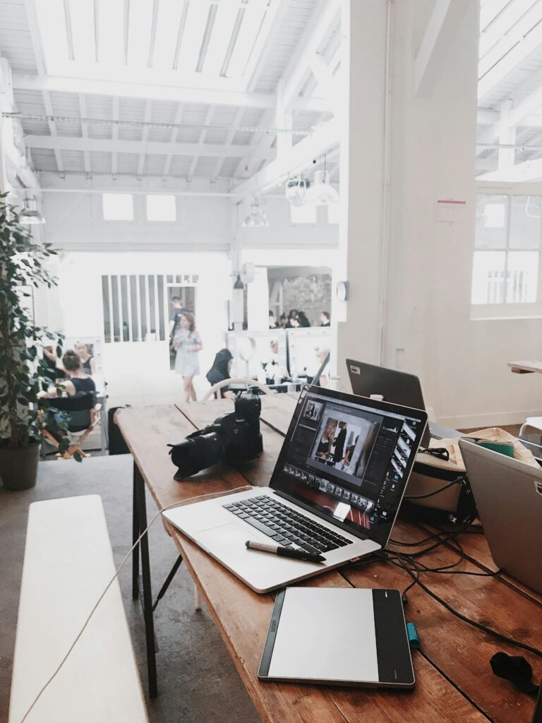 A bright, modern workspace featuring laptops, a camera, and a drawing tablet in an indoor office.